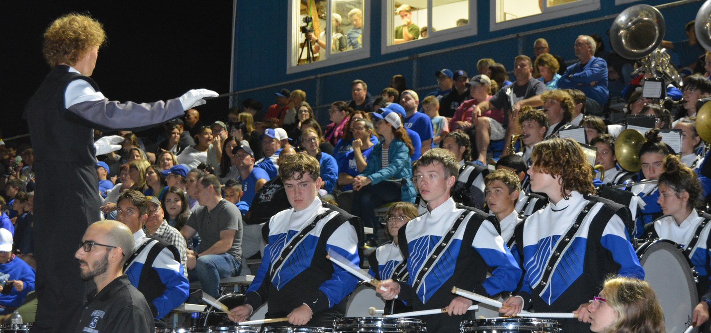 Drum major conducting the Blue Knights Marching Band drumline in the stands at a Southington High School football game